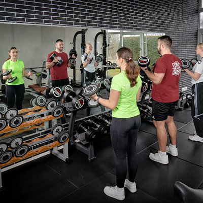 Frau und Mann beim Krafttraining mit Kurzhanteln vor einer Spiegelwand bei active Therapie und Training.
